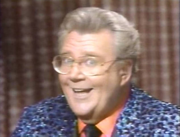 Rod is wearing a blue leopard-print jacket, orange shirt & black tie